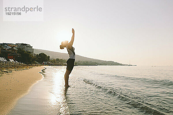 Frau mit gefalteten Händen praktiziert Yoga an einem sonnigen Tag am Strand