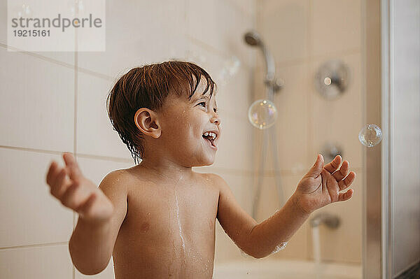 Fröhlicher Junge spielt mit Seifenblasen in der Badewanne