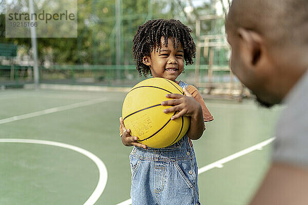 Smiling son holding basketball and talking to father on sports court