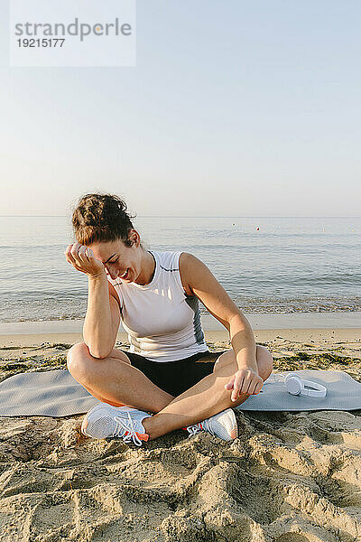 Glückliche Frau sitzt auf einer Trainingsmatte vor dem Meer