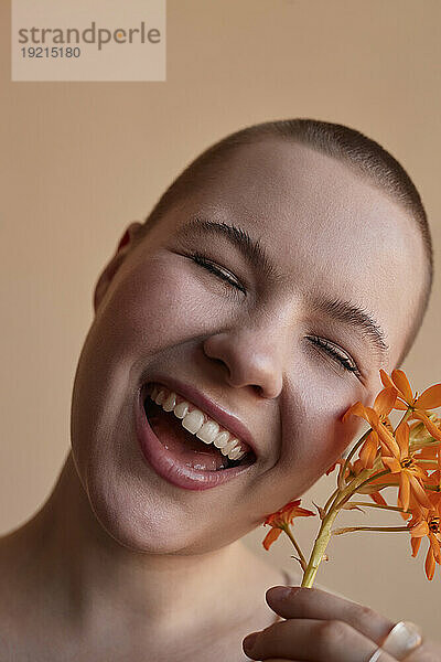 Lachende junge Frau hält Blume vor beigem Hintergrund