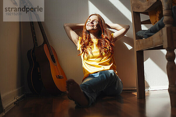 Smiling redhead woman with hands behind head sitting on floor