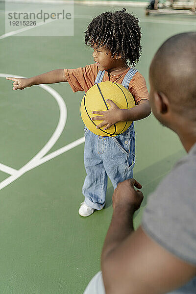 Vater und Sohn halten Basketball in der Hand und zeigen auf den Sportplatz