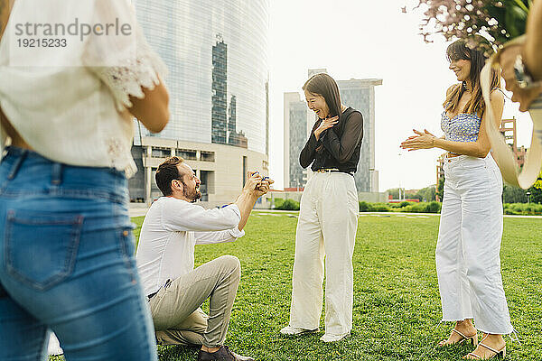 Happy man proposing woman with ring in front of buildings
