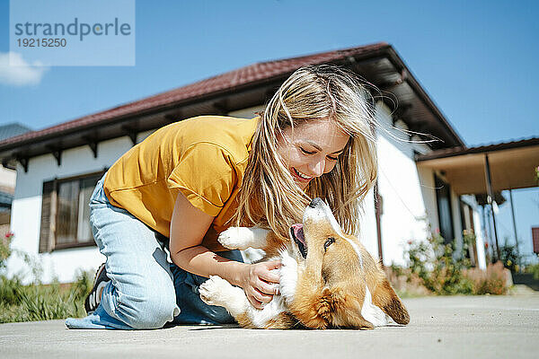 Glückliche Frau  die an einem sonnigen Tag mit einem Corgi-Hund vor dem Haus spielt