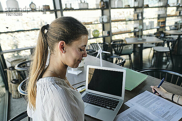 Porträt einer hübschen Blondine  die am Cafétisch an Dokumenten arbeitet