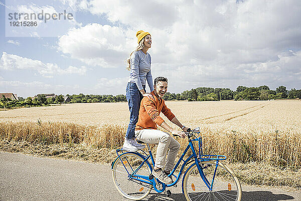 Lächelnder reifer Mann gibt Frau auf dem Feld eine Fahrradtour
