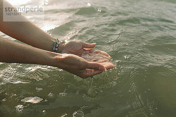 Frau hält Wasser mit hohlen Händen am Strand