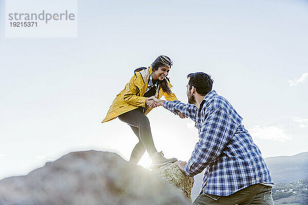 Lächelnde Frau hilft Mann beim Klettern auf Felsen
