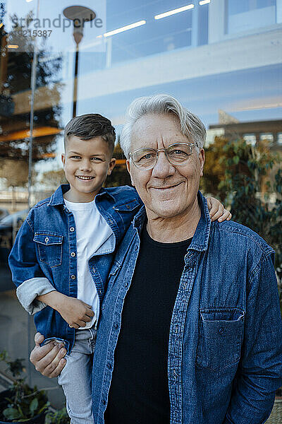 Smiling senior man with grandson standing near wall