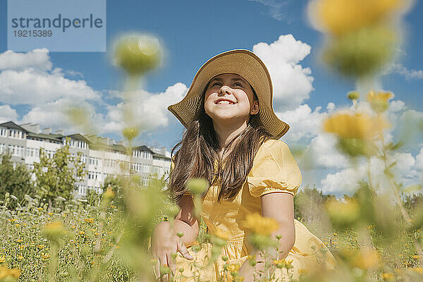Nachdenkliches Mädchen mit Hut im Blumenfeld an einem sonnigen Tag