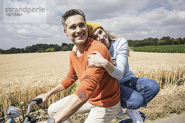 Lächelnde Frau umarmt Mann auf Fahrrad an sonnigem Tag