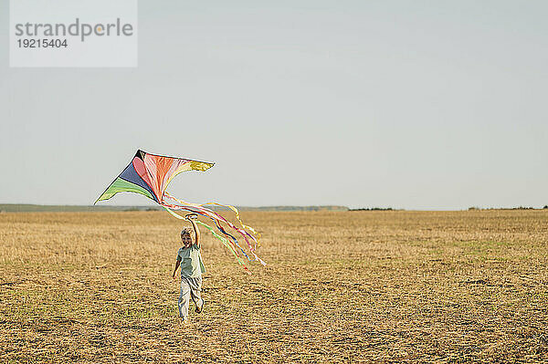 Cheerful boy flying kite and running in meadow