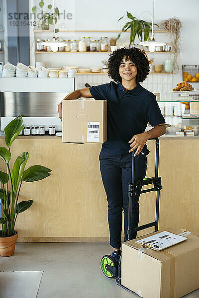 Lächelnde Lieferfrau trägt Paket und steht im Café
