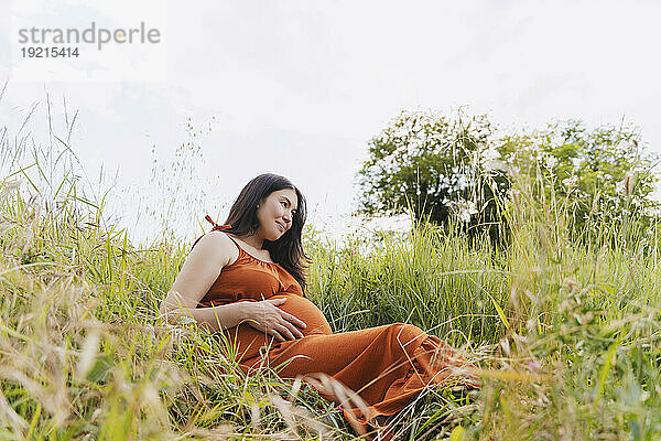 Schwangere Frau sitzt auf Gras unter dem Himmel