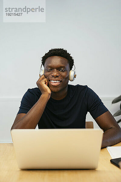 Fröhlicher Student mit kabellosen Kopfhörern sitzt am Laptop