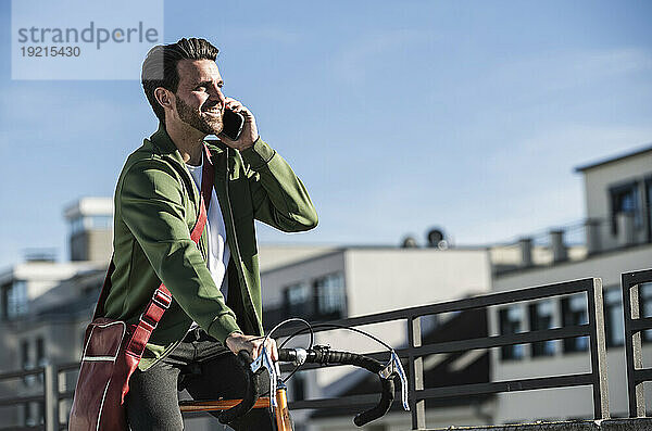 Lächelnder Mann  der auf dem Smartphone spricht und Fahrrad fährt