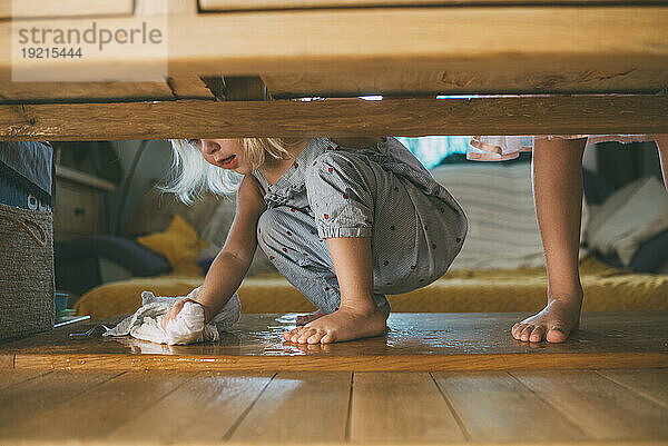 Girl wiping water with rag on hardwood floor at home