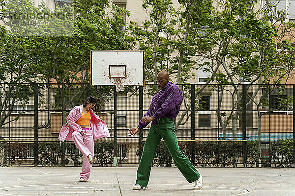 Frau tanzt mit nicht-binärer Person auf Basketballplatz