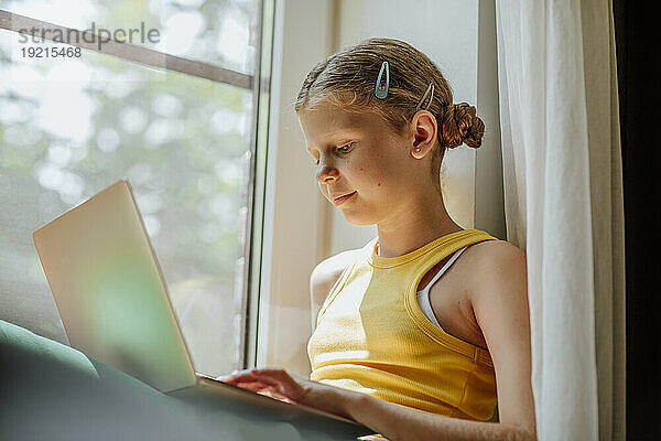 Mädchen benutzt Laptop am Fenster zu Hause
