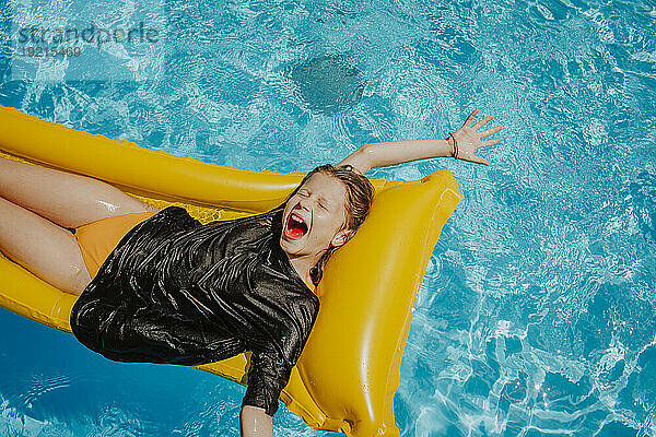 Fröhliches Mädchen schreit und liegt auf der Luftmatratze im Schwimmbad