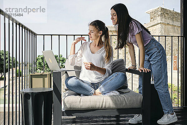 Zwei junge Frauen benutzen Laptop auf dem Balkon