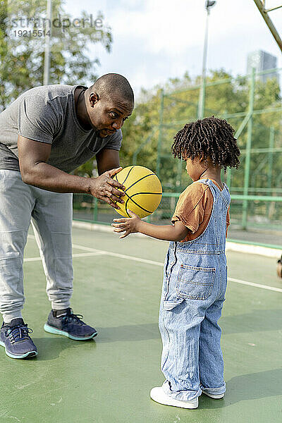 Vater gibt seinem Sohn Basketball auf dem Sportplatz