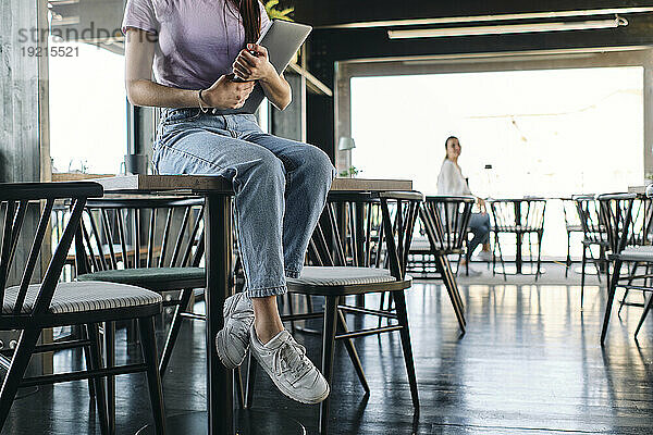 Low section of young woman sitting on top of cafe table with laptop in hands