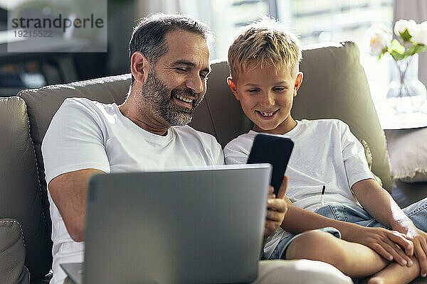 Lächelnder Vater teilt Smartphone mit Sohn im Wohnzimmer