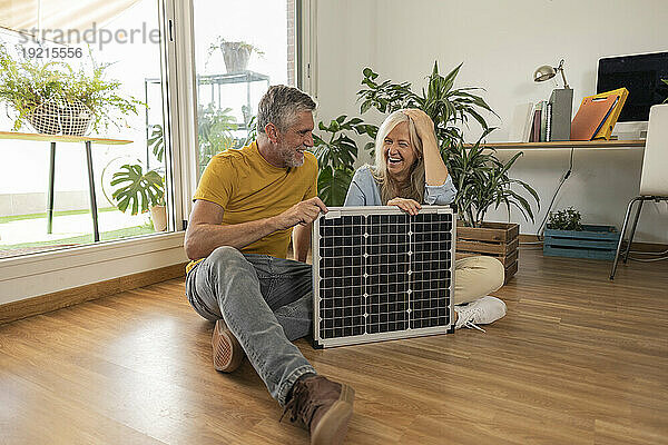 Glückliches Paar sitzt mit Solarpanel zu Hause