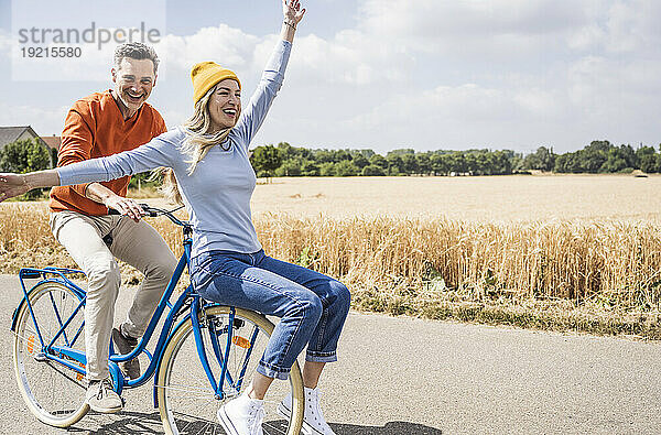 Glücklicher reifer Mann  der einer Frau vor dem Feld eine Fahrradtour gibt