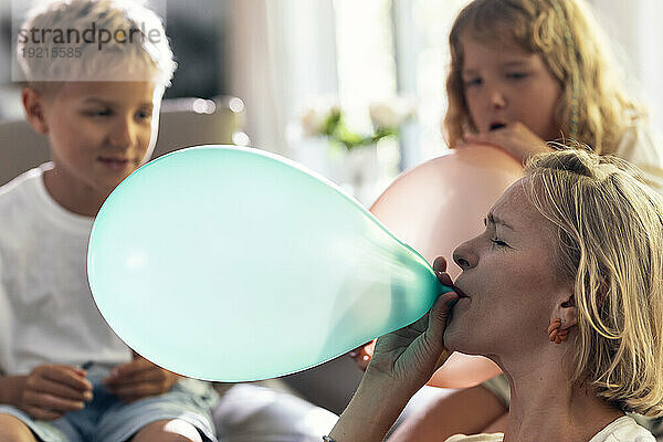 Mutter bläst Ballon mit Kindern zu Hause