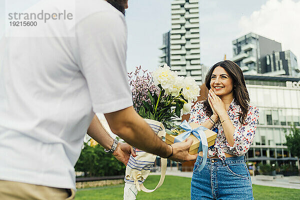 Mann schenkt einer glücklichen Frau eine Geschenkbox und einen Blumenstrauß