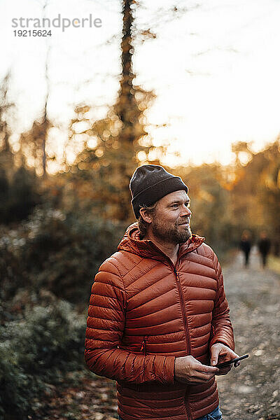 Nachdenklicher Mann hält Smartphone im Wald