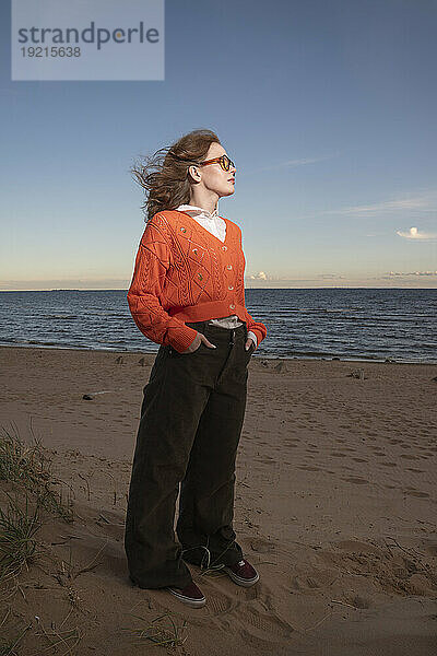 Junge Frau mit Sonnenbrille steht am Strand