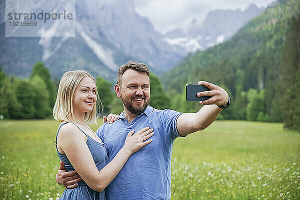 Lächelnder Mann macht Selfie per Smartphone mit Frau