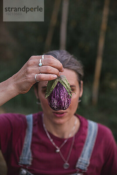 Frau hält Aubergine vor Gesicht