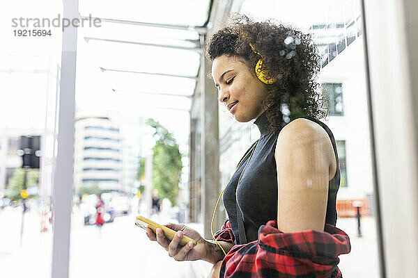 Glückliche Frau trägt Kopfhörer und benutzt Smartphone in der Stadt