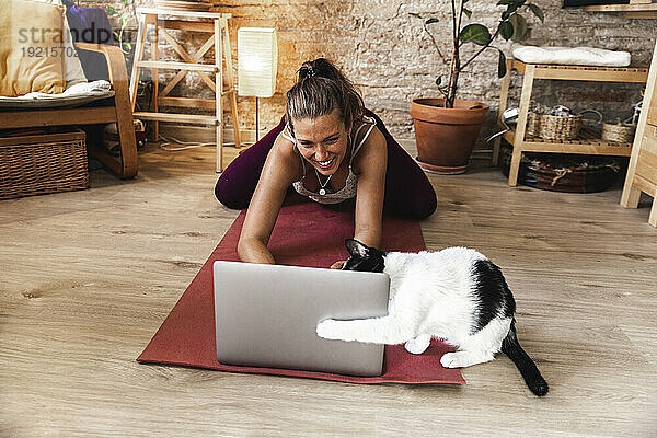 Lächelnde Frau benutzt Laptop und spielt zu Hause mit Katze