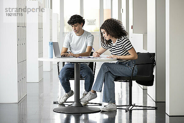 Student benutzt Laptop mit Freund  der am Tisch in der Universität schreibt