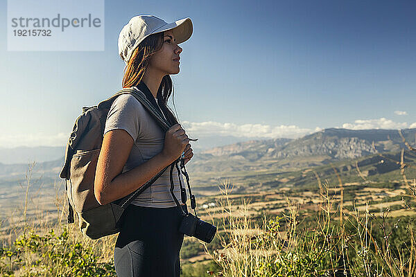 Junge Frau mit Rucksack und Kamera beim Wandern an einem sonnigen Tag