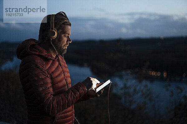 Reifer Mann hört Musik über sein Smartphone in der Nähe des Sees