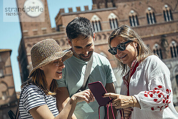 Fröhliche Touristen  die an einem sonnigen Tag ihr Smartphone teilen
