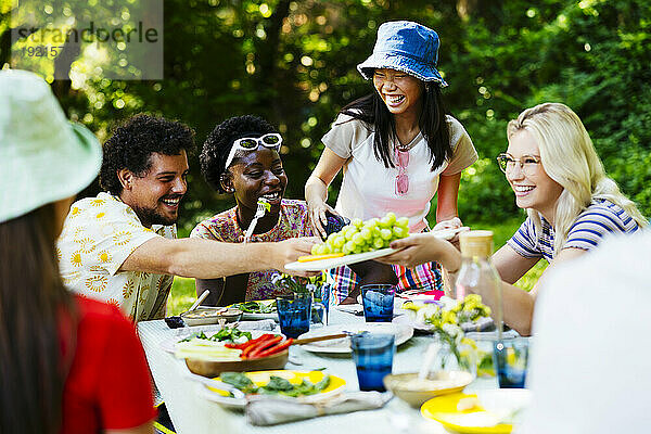 Glückliche Frau bietet Freunden am Picknicktisch Weintrauben an