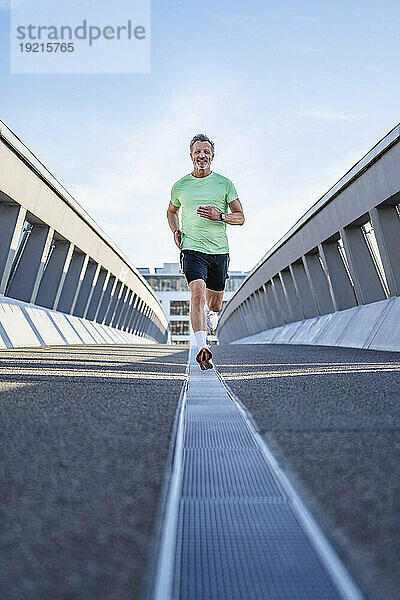 Reifer Sportler joggt auf der Fußgängerbrücke vor dem Himmel