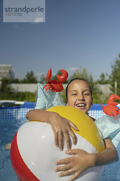 Lächelndes Mädchen hält Ball im Schwimmbad