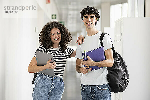 Glückliche Studenten halten Aktenordner und Laptop im Flur
