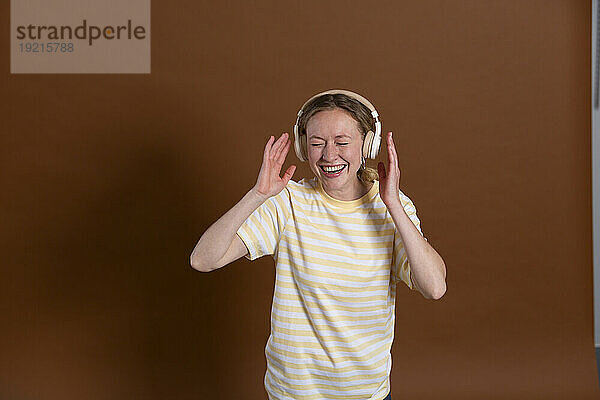 Frau lacht und hört Musik über Kopfhörer vor braunem Hintergrund