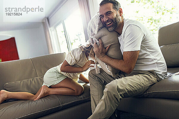Happy father enjoys playing with daughter on sofa