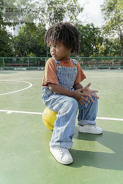 Junge sitzt auf Basketball auf Sportplatz